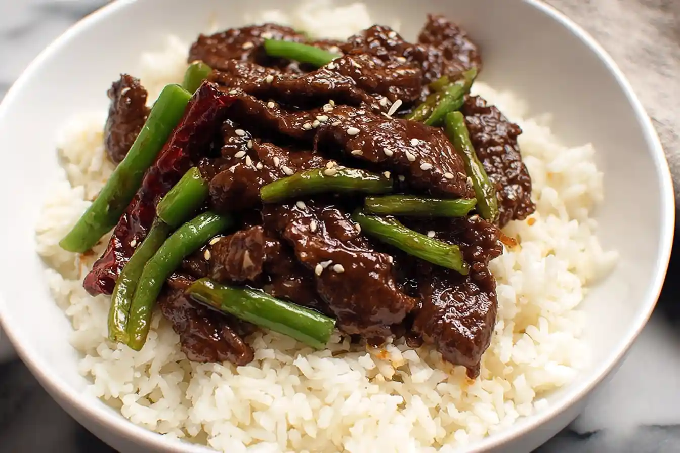 A close-up shot of a plate of savory Mongolian Beef, garnished with green onions and sesame seeds.