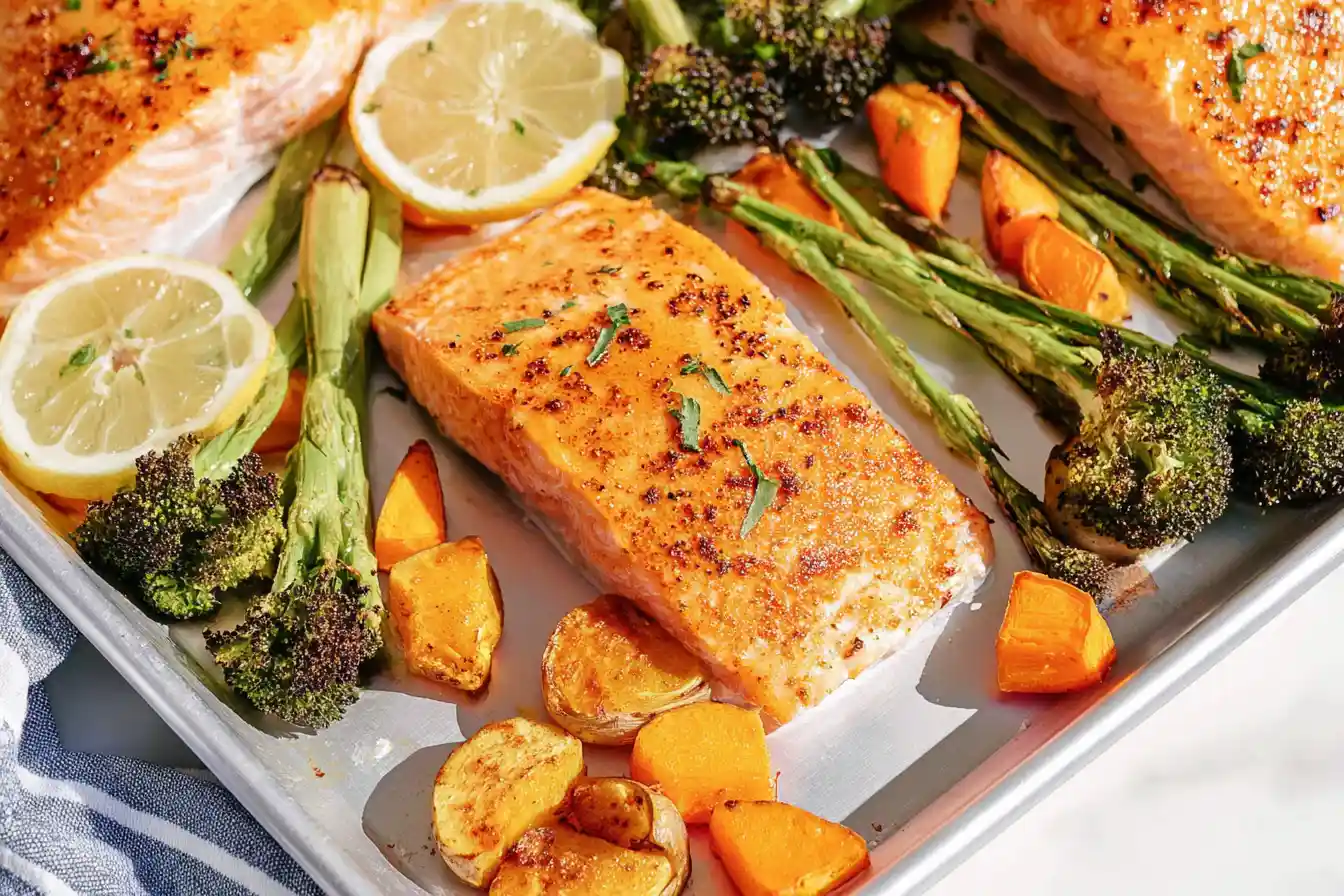 A close-up shows perfectly cooked Sheet Pan Maple Dijon Glazed Salmon fillets alongside roasted broccoli and sweet potatoes, garnished with fresh herbs.