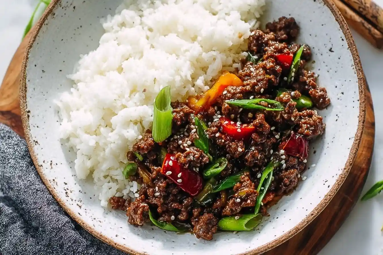 A close-up of a Korean Ground Beef Bowl in a rustic ceramic dish, served with a side of fluffy white rice and garnished with scallions.