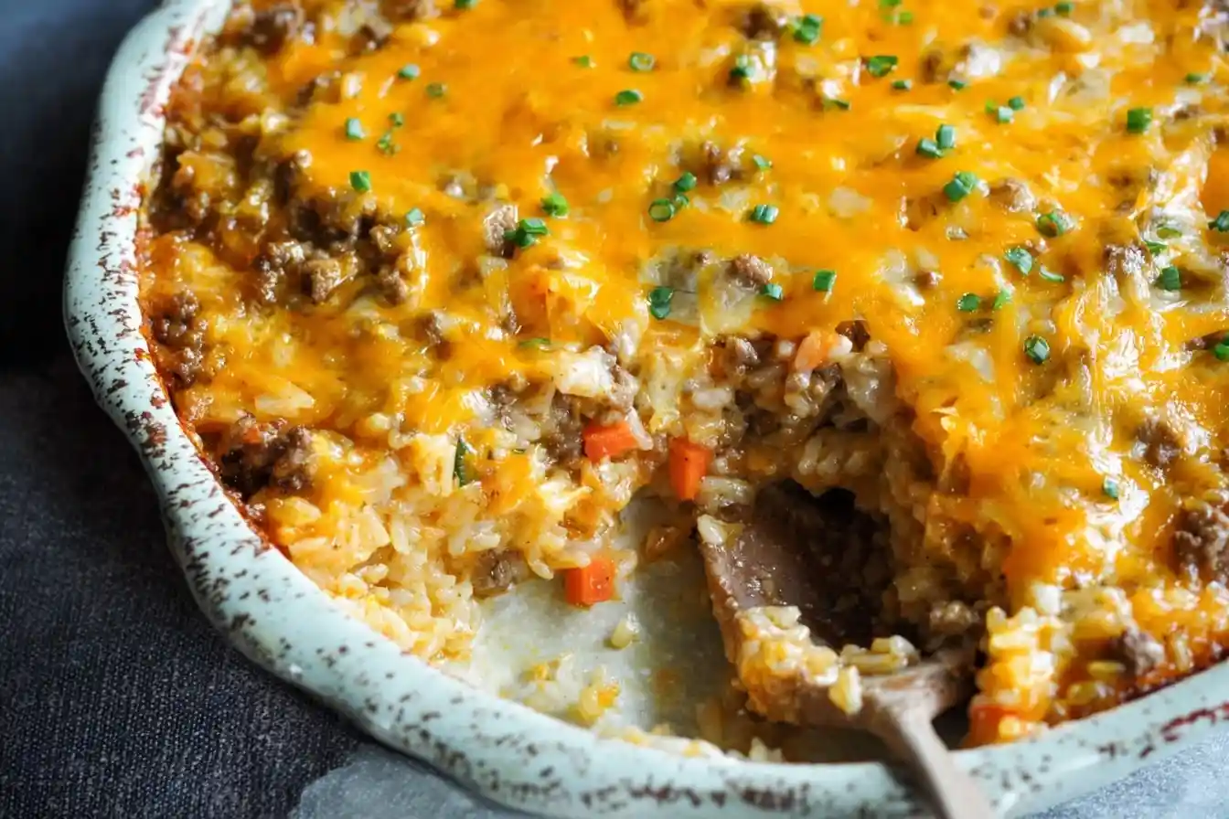 A close-up of a cheesy beef and rice casserole in a baking dish, with a spoonful scooped out to show the inside.