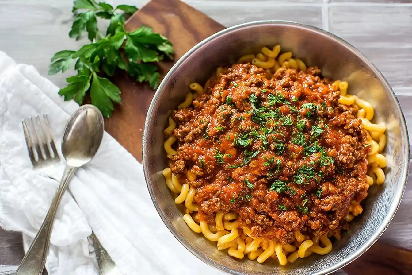 A close-up of a metal bowl filled with corkscrew pasta and topped with a generous portion of rich, homemade meat sauce.