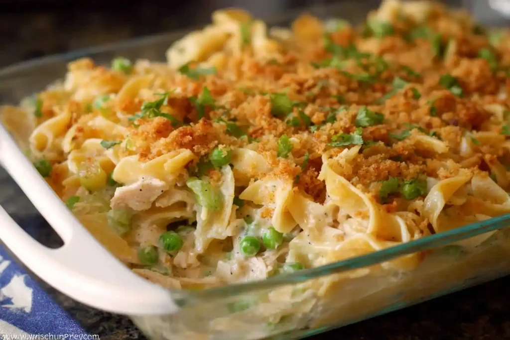 A close-up of a classic Tuna Noodle Casserole in a glass baking dish, topped with golden breadcrumbs and fresh parsley.