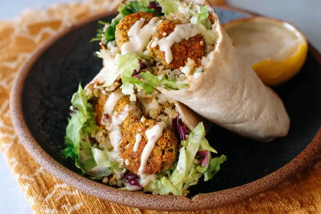 Close-up of a delicious Falafel Wrap cut in half, filled with crispy falafel and greens, drizzled with sauce.