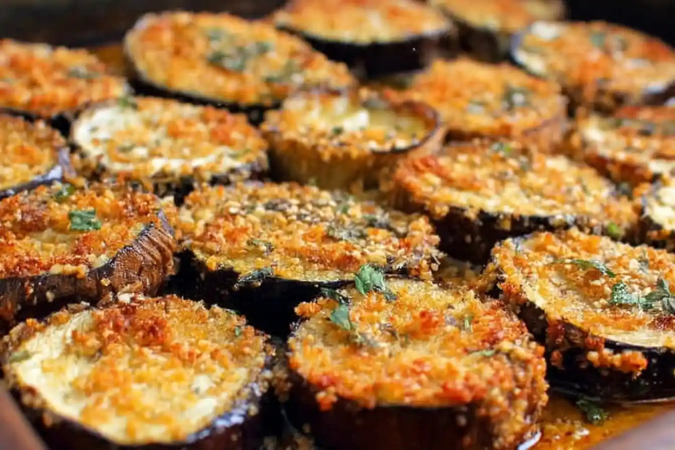 Close-up view of golden brown Crispy Baked Eggplant slices topped with herbs on a baking sheet