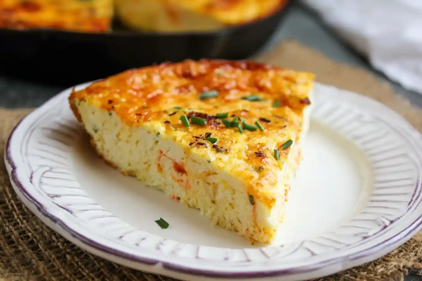 Slice of fluffy Crustless Quiche with cheese and chives served on a white plate.