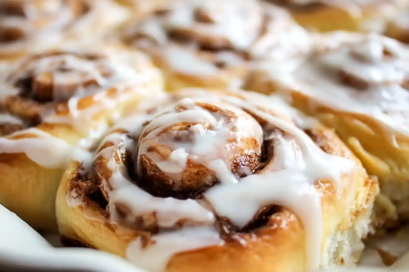 A close-up shot of warm, gooey cinnamon rolls fresh from the oven and topped with a sweet white icing.