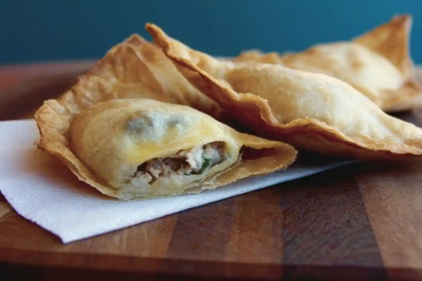 Golden brown fried wontons on a wooden board, with one bitten open to show the savory meat filling.