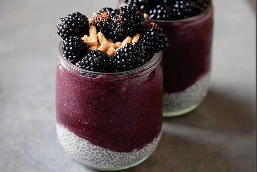 Close-up of a layered blackberry chia pudding in a glass jar, topped with fresh blackberries and crunchy nuts.