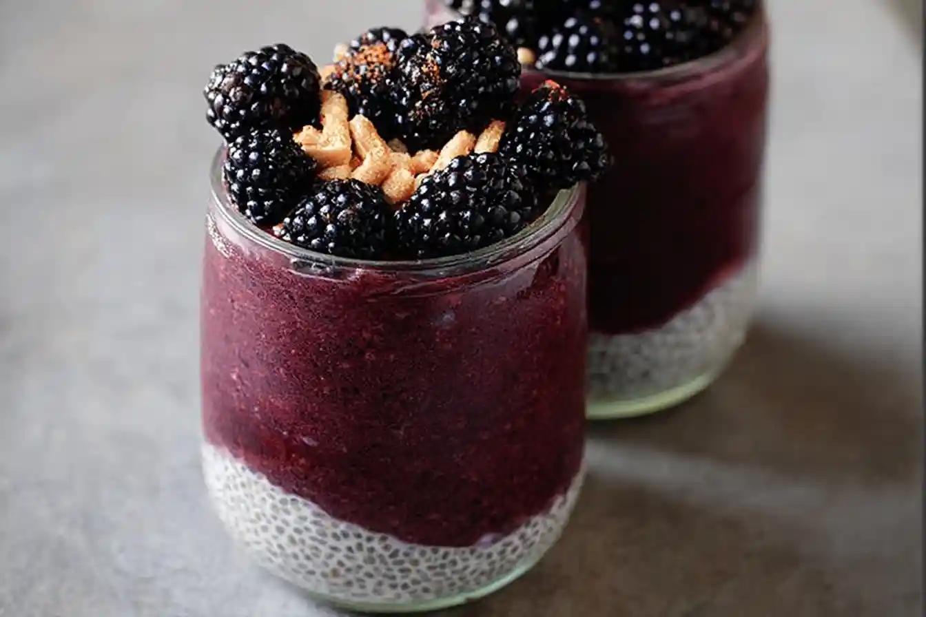 Close-up of a layered blackberry chia pudding in a glass jar, topped with fresh blackberries and crunchy nuts.