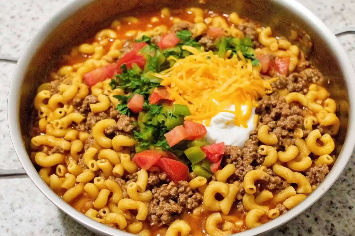 Overhead view of a skillet filled with Taco Pasta, topped with cheese, tomatoes, and sour cream.