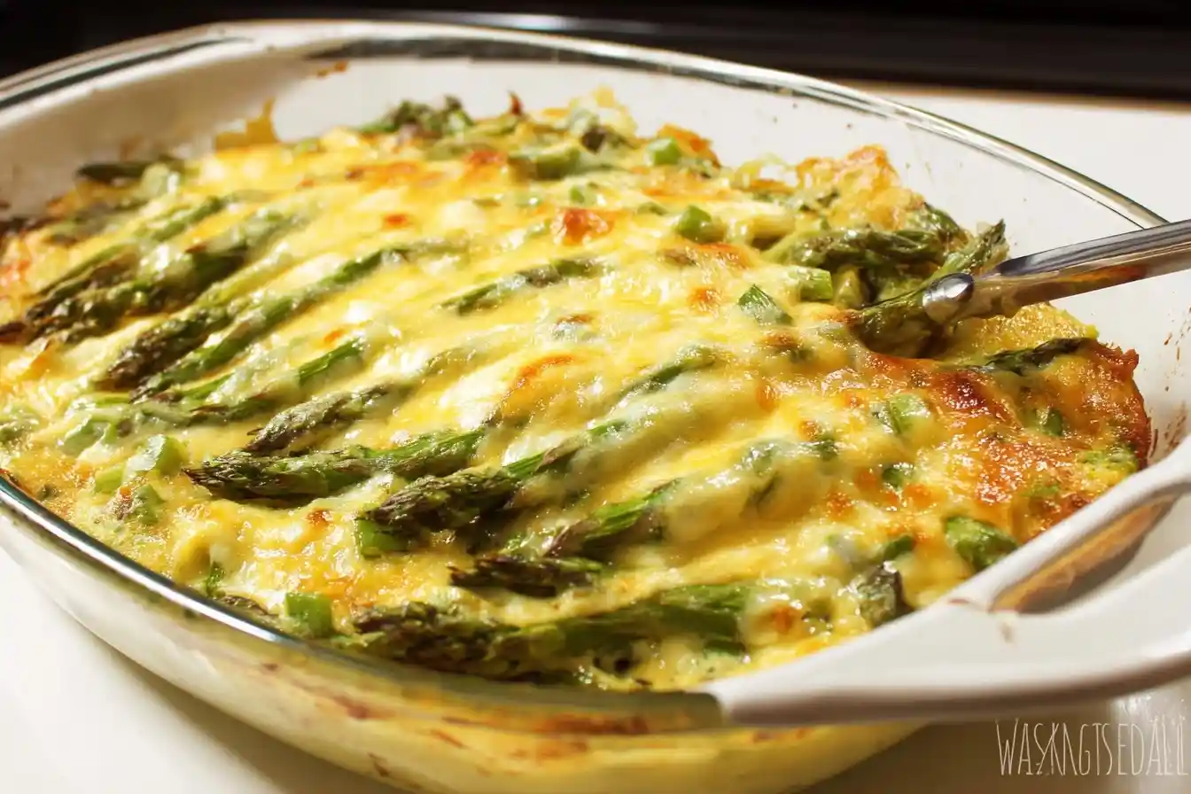 A freshly baked cheesy asparagus casserole in a glass dish topped with melted golden brown cheese.